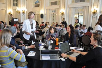 Small groups at Marketing Matters conferred about best practices and strategies for collaboration. Woman standing talking to a group of people at a table